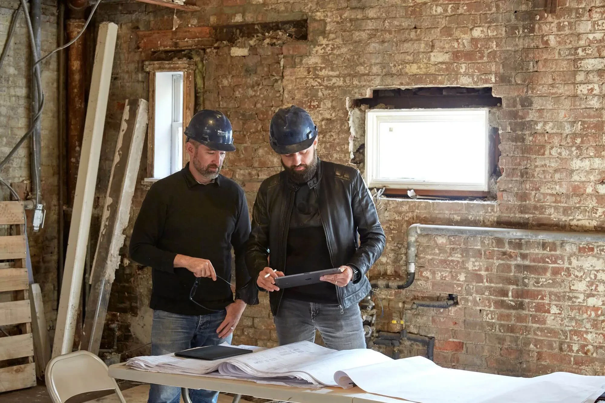 Ruslan Bukharin reviewing architectural blueprints at luxury residential renovation site with exposed brick walls